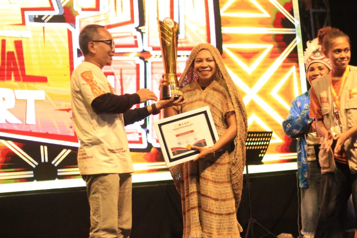 Ketua Dekranasda Kabupaten Deiyai, Fransina Rumbiak Mote, menunjukkan piala Juara Umum Festival Timika Inside Festival of Art (TIFA) 2026 yang berhasil diraih untuk kedua kalinya secara berturut-turut.